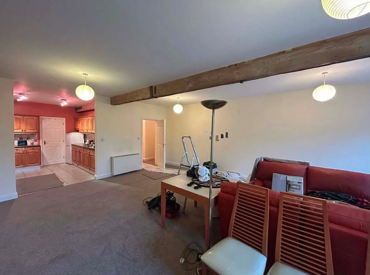 Open-plan living room before decorating, with plain cream walls under an oak beam