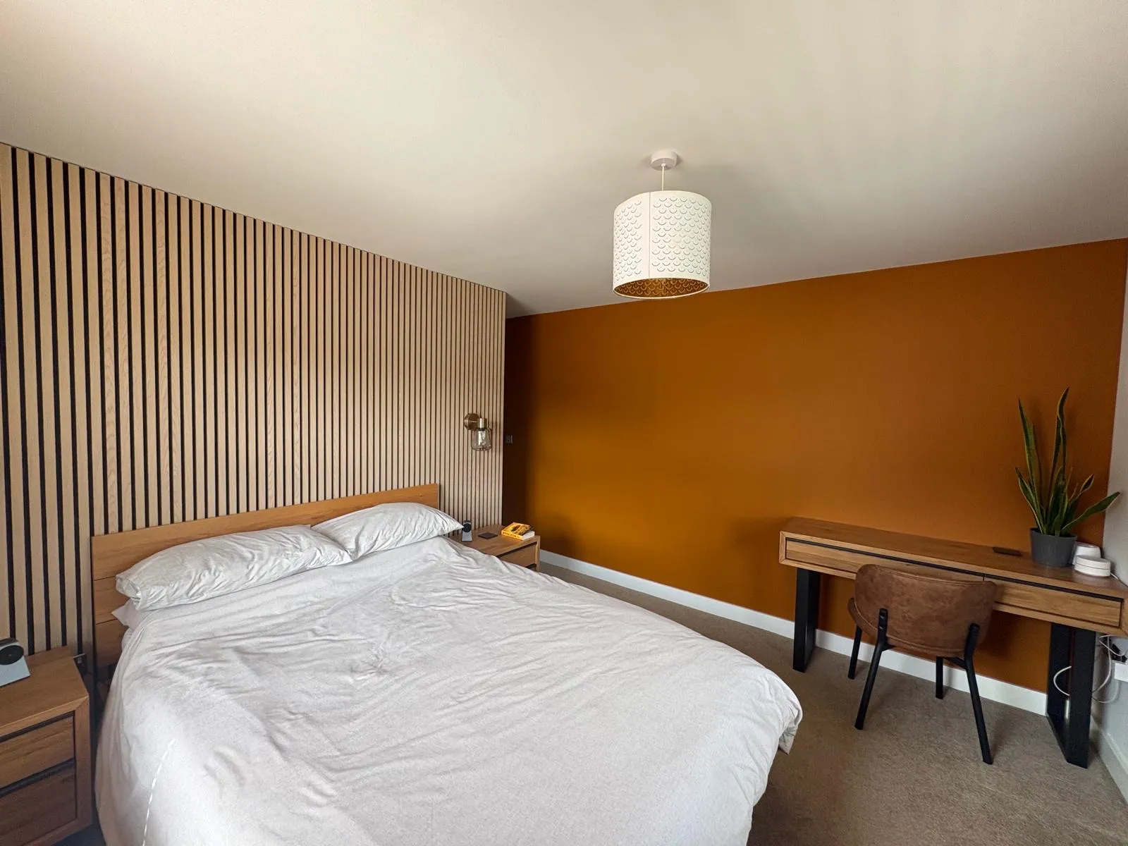 Bedroom with a full-height oak slat panelled wall and a burnt orange feature wall