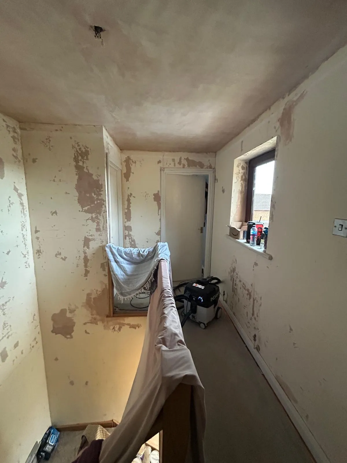 Bedroom stripped back to patchy bare plaster with dust sheets down