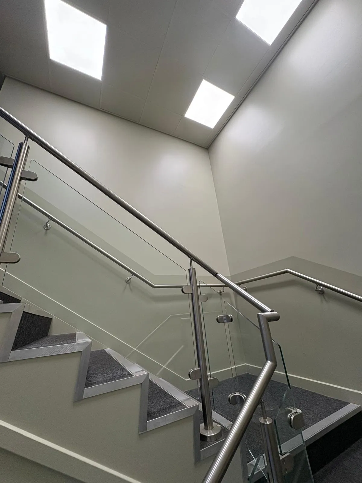 Looking up a commercial stairwell with a glass balustrade and recessed ceiling lights