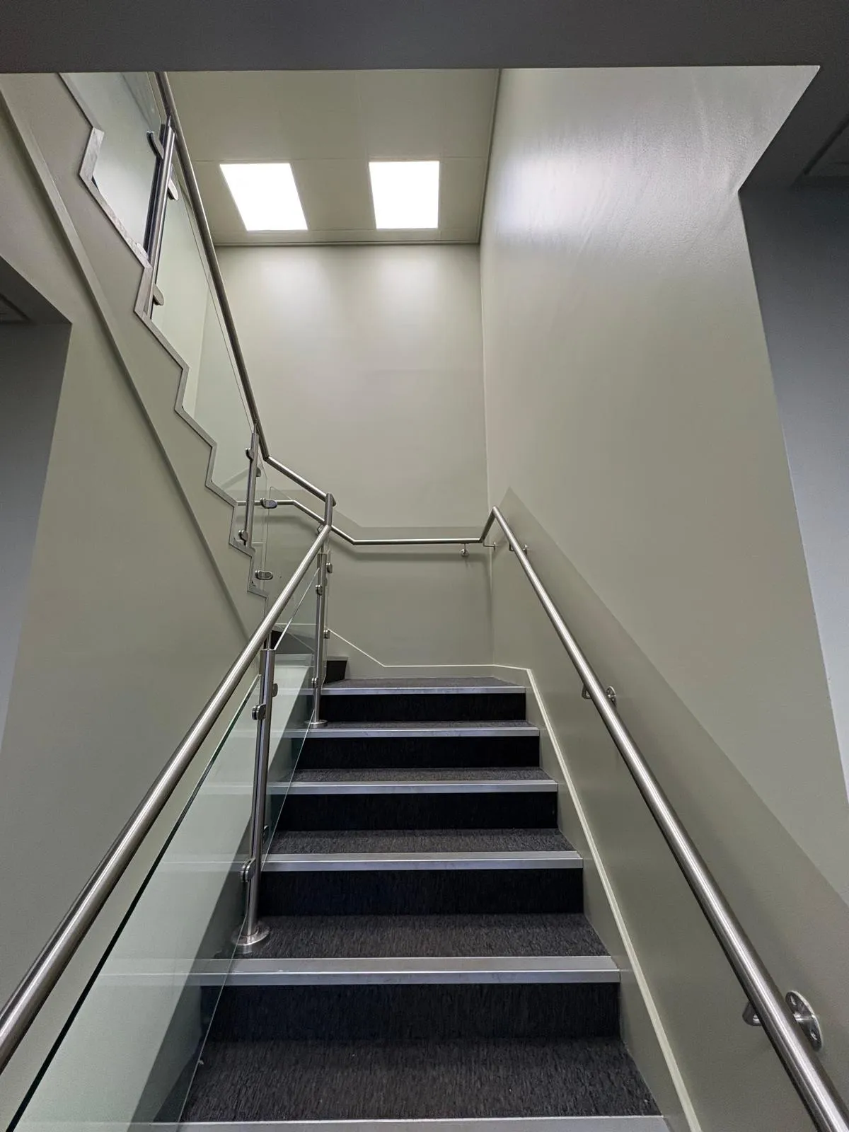 Commercial stairwell decorated in a soft neutral with a glass balustrade and stainless handrail