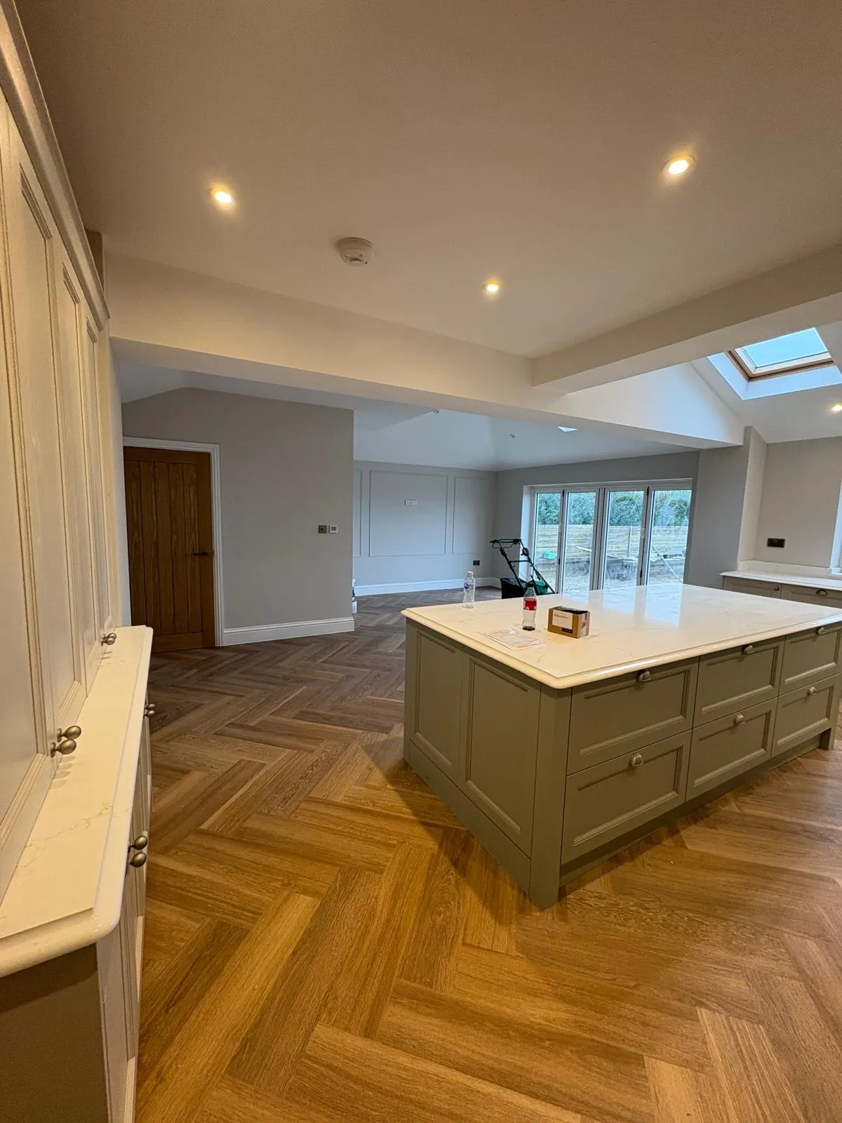 Open-plan kitchen with a sage green island, white worktops and herringbone parquet flooring