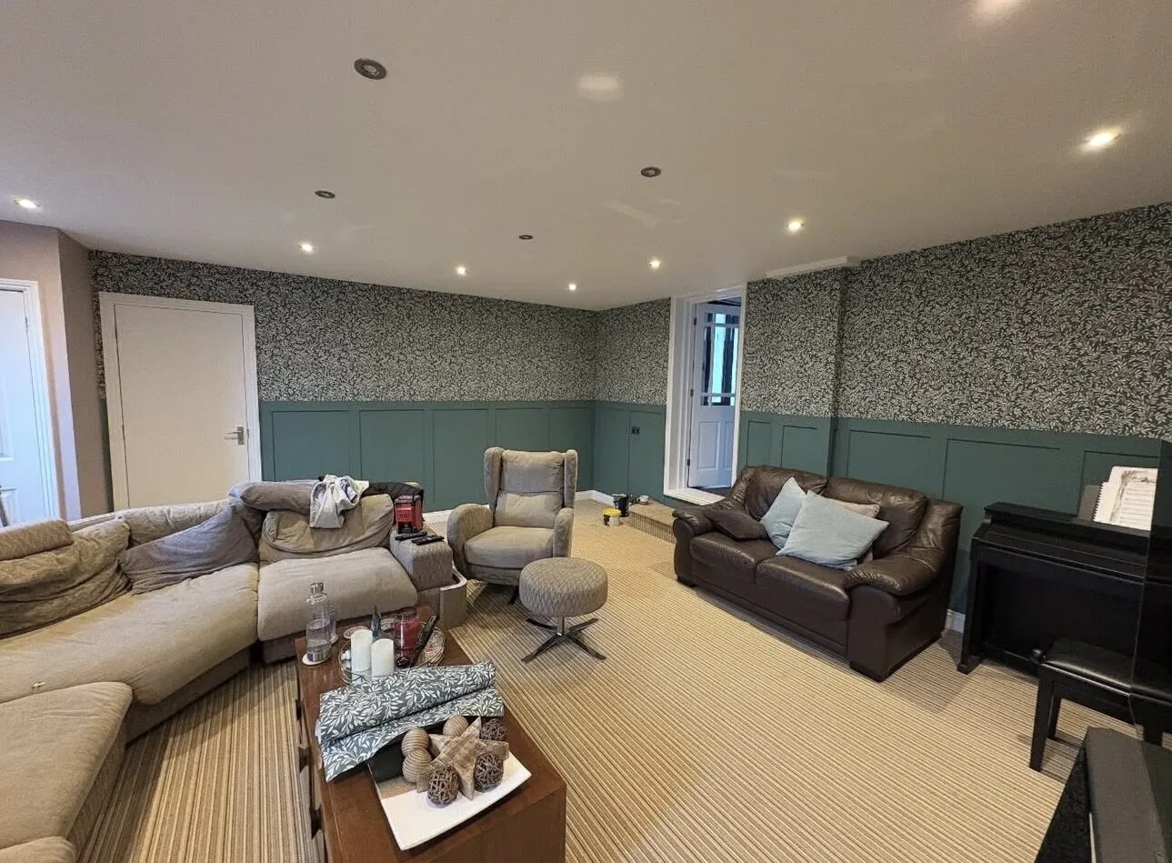 Living room with deep green wall panelling below patterned botanical wallpaper