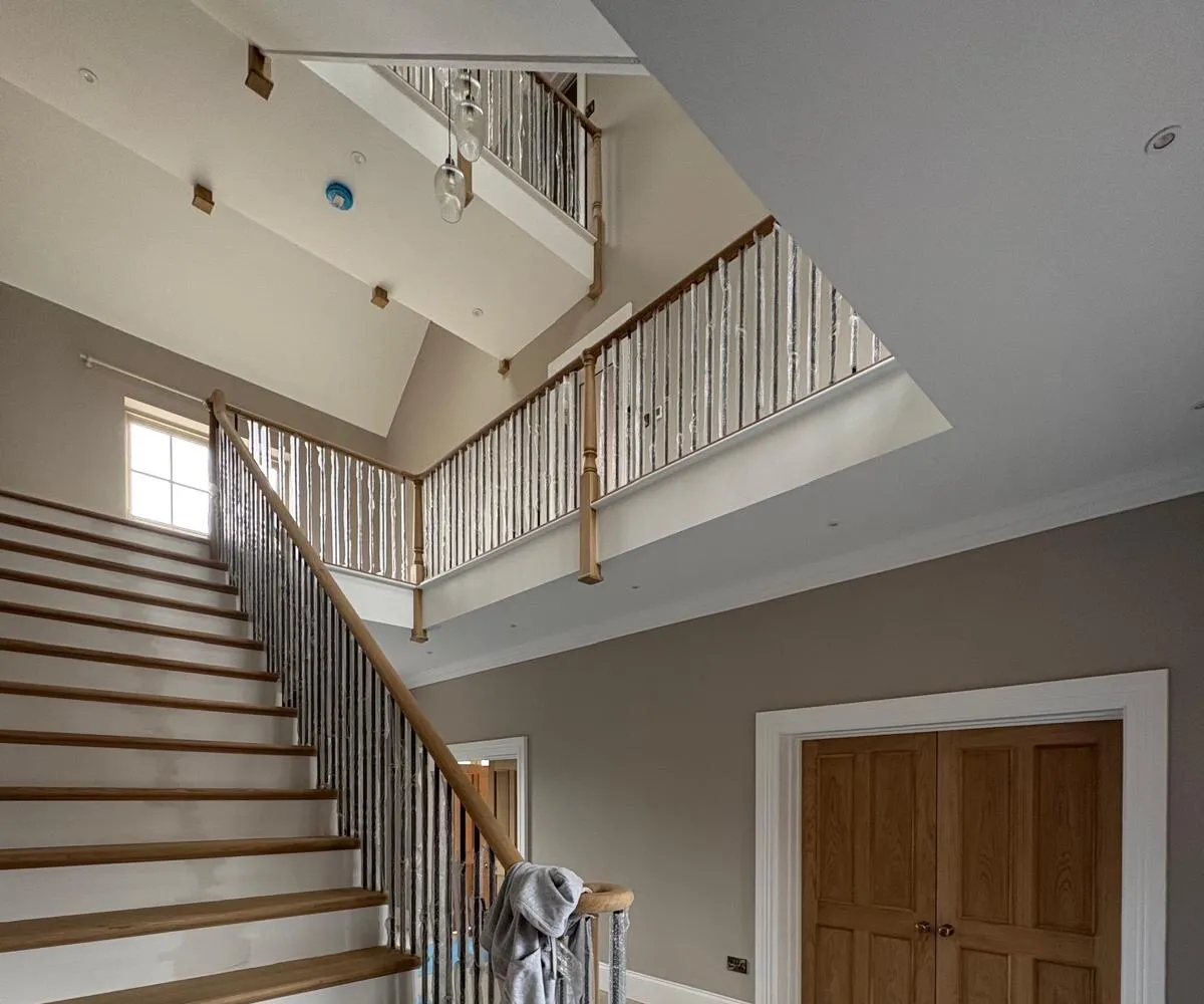 Double-height hallway mid-decoration — oak staircase with spindles masked for a flawless finish