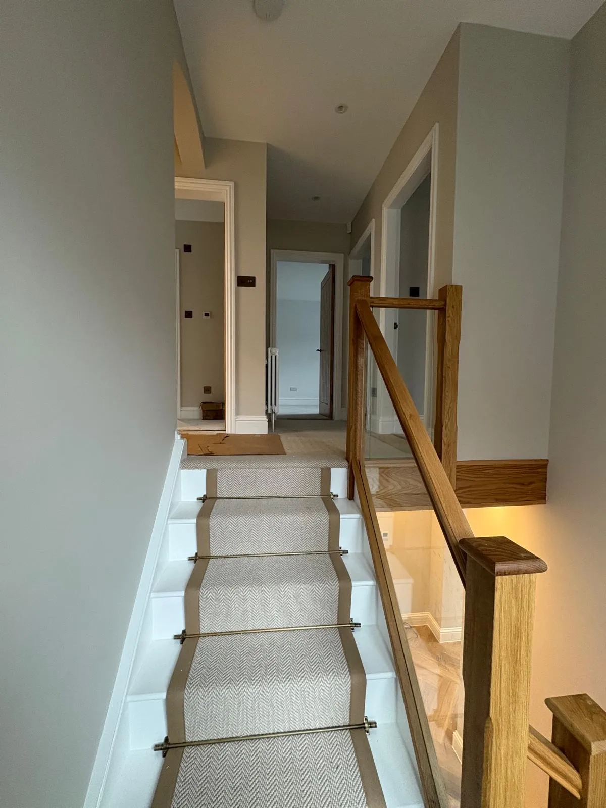 Staircase painted white with an oak handrail and a natural carpet runner