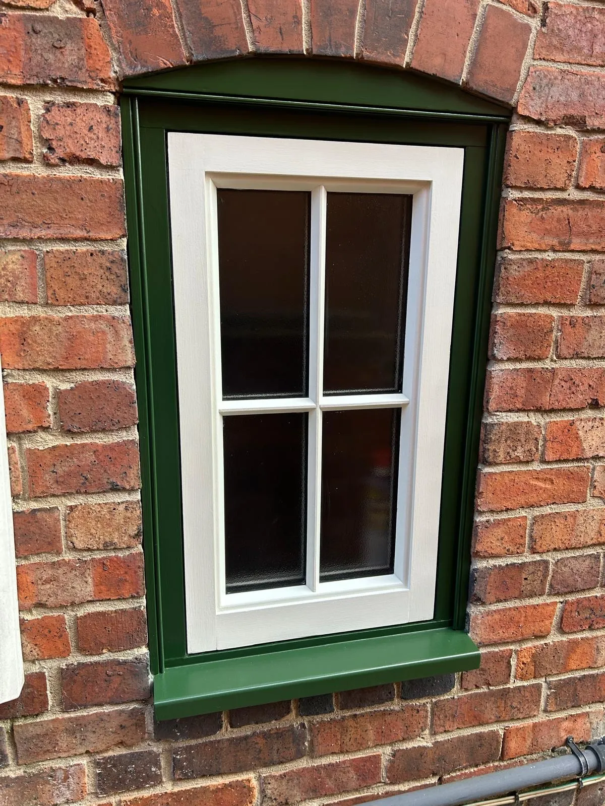 Timber casement window with a deep green frame and cill against red brickwork